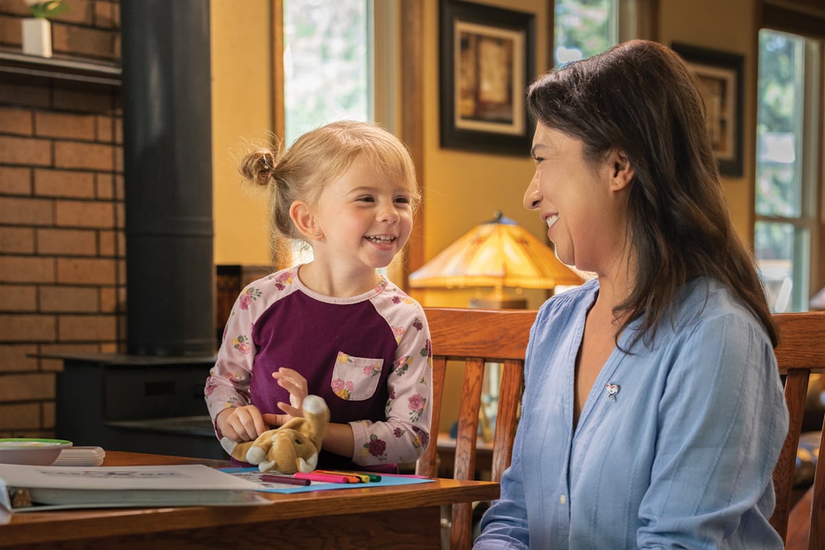 Young girl with plush toy looks and smiles at woman